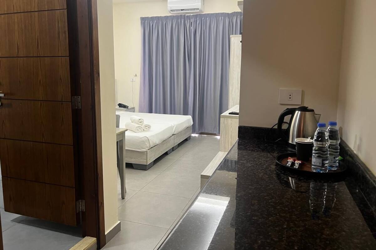 A hotel room with a bed, a bathroom, and a counter with a kettle and water bottles.