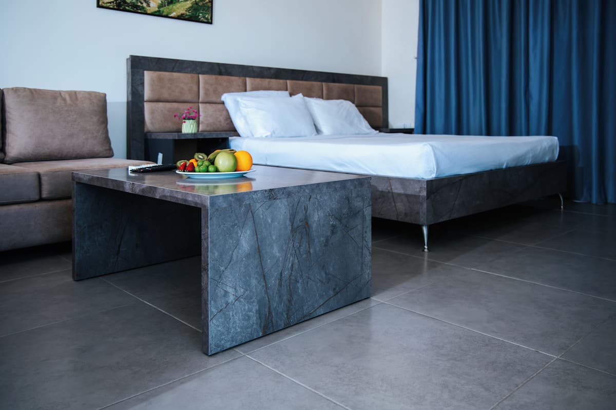 A modern hotel room with a bed, a sofa, a marble coffee table, and a fruit bowl.