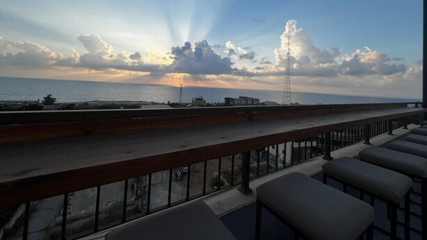 Un balcon avec vue sur la mer et une haute tour qui se profile à l’horizon.