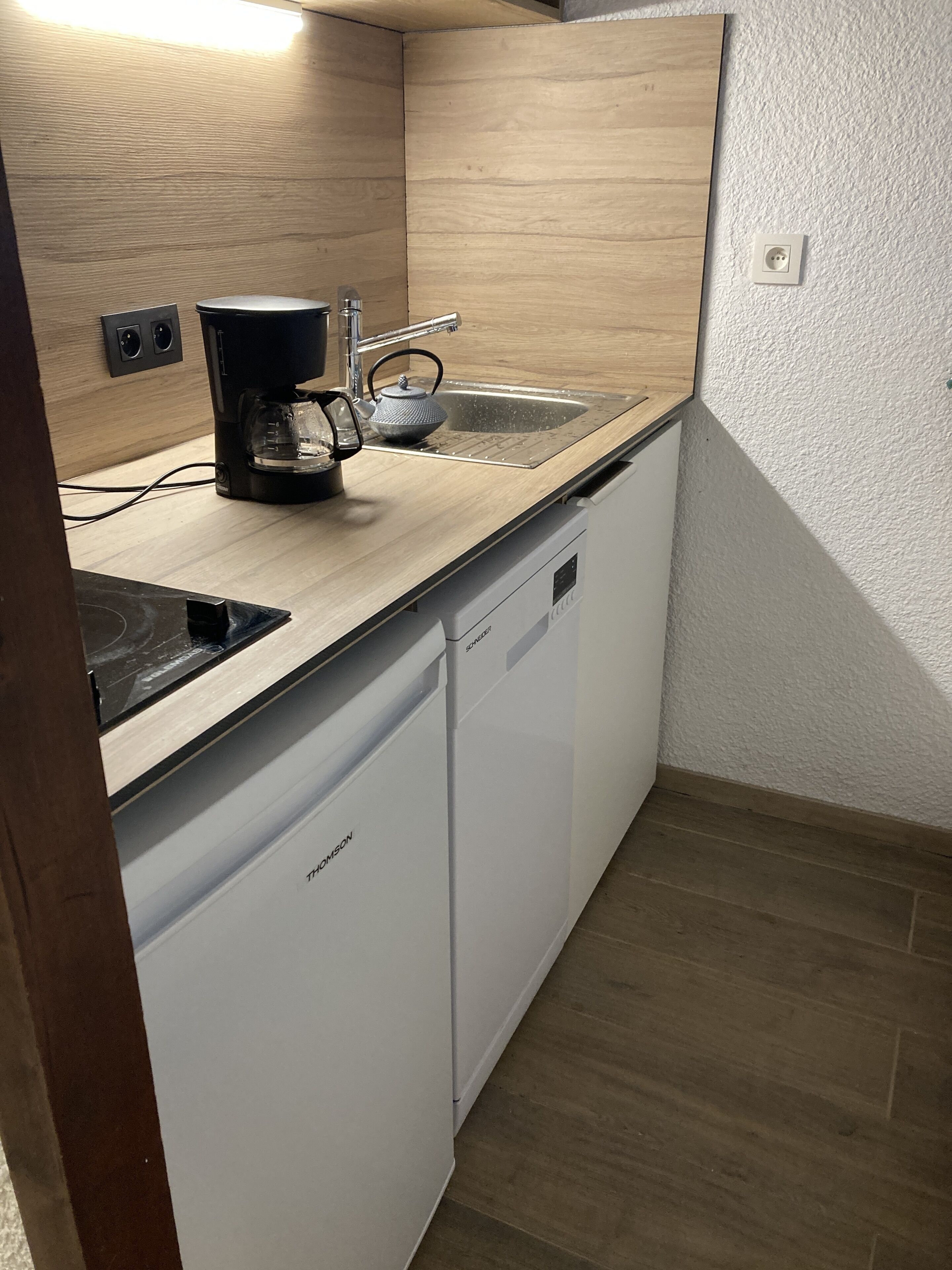 Una cocina compacta con lavavajillas, cafetera y fregadero.