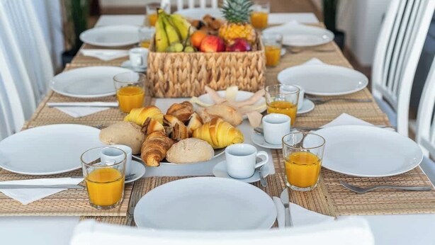 Une table mise pour le petit-déjeuner, avec un panier de fruits, des croissants et des verres de jus.