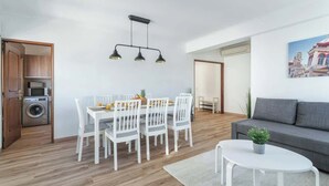 Un salon moderne comprenant un coin repas, un canapé gris, une table basse blanche et un tableau accroché au mur.