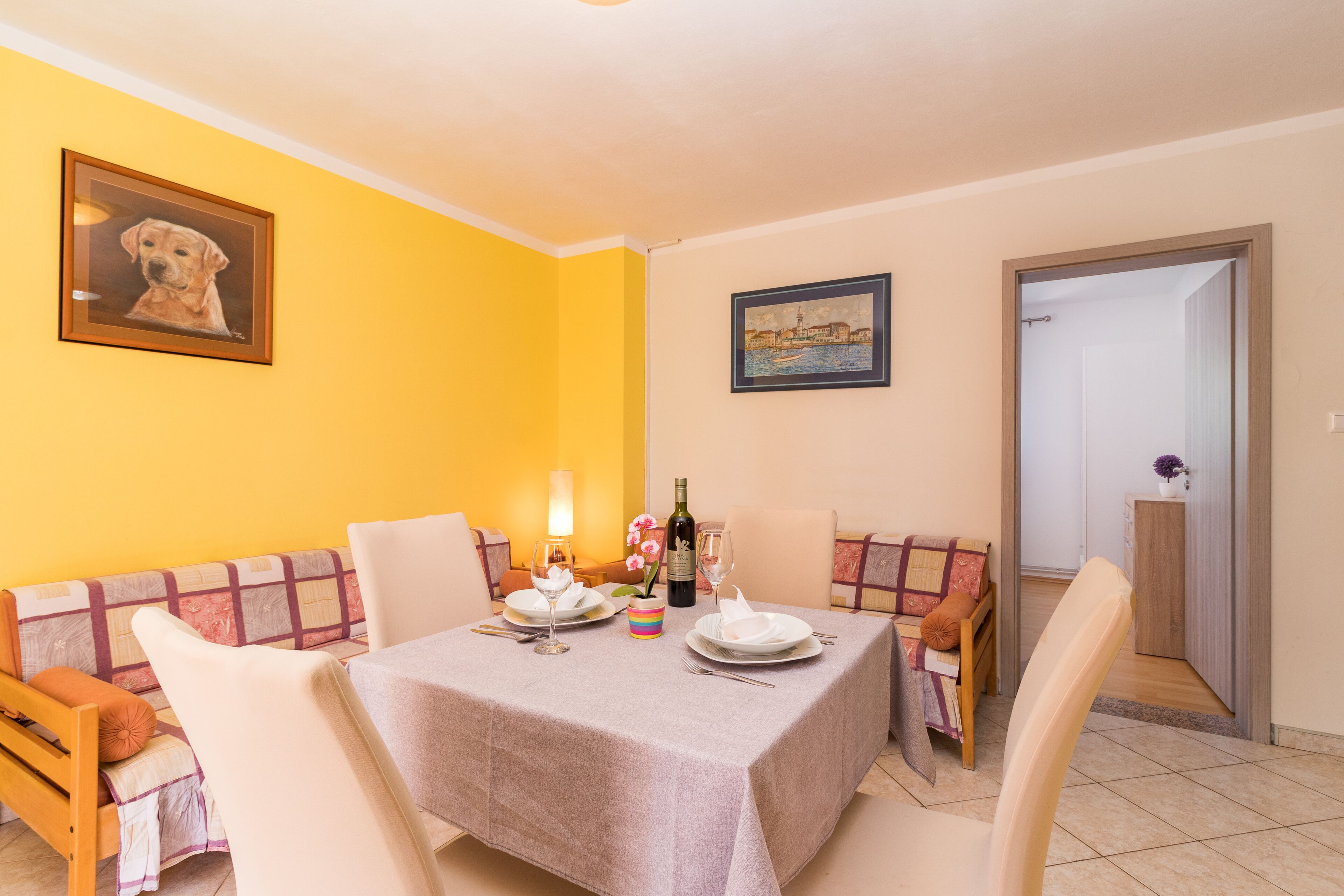 A dining area with a table set for two, a sofa, and a door leading to another room.