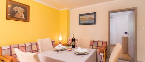 A dining area with a table set for two, a sofa, and a door leading to another room.