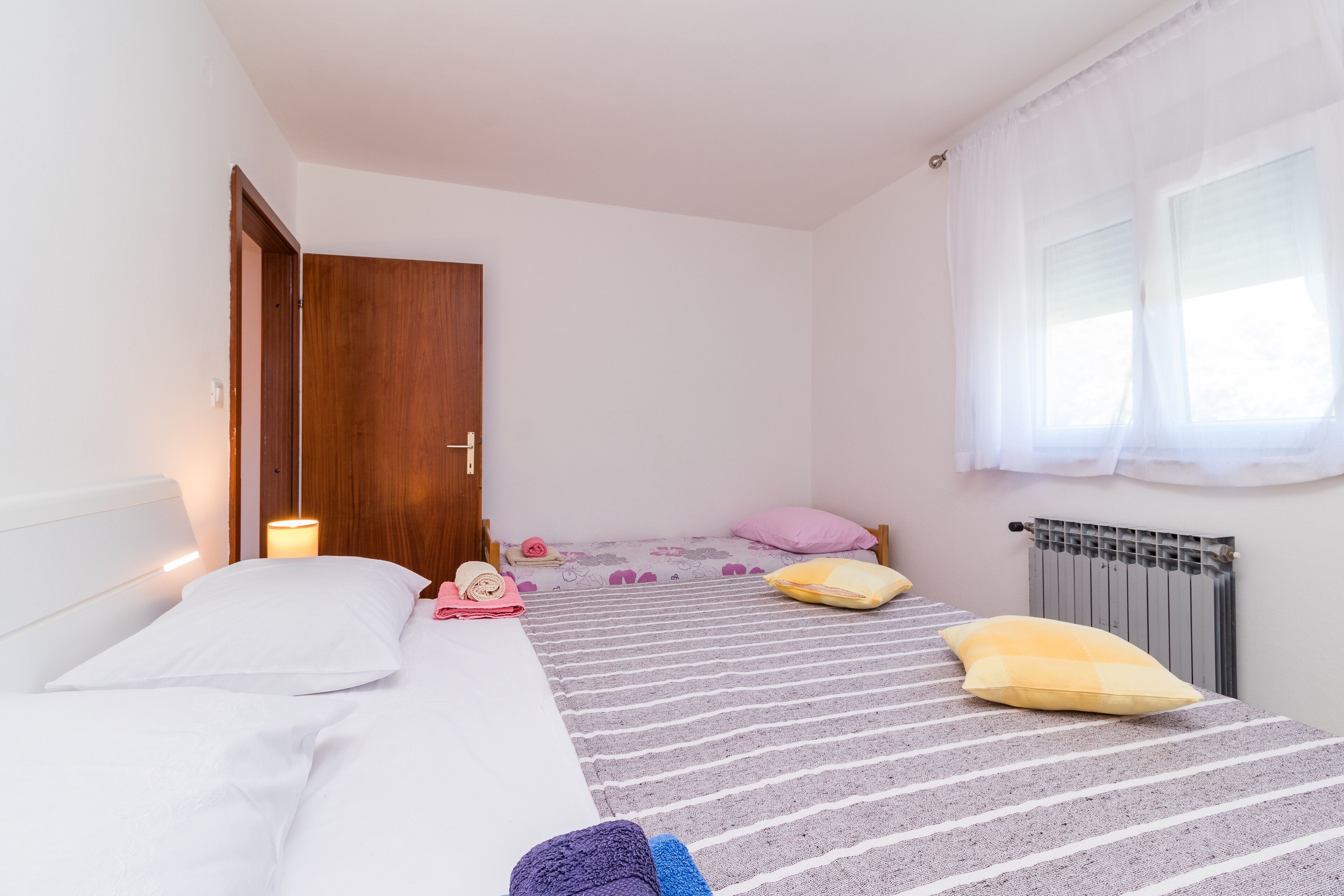 A bedroom with two beds, a wooden door, a radiator, and a window with curtains.
