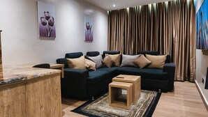 A modern living room with a sectional sofa, a wooden coffee table, and a flat-screen TV mounted on the wall. - Sunflower Residence Victoria Island (Lagos)