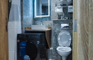 A compact bathroom with a washing machine, a toilet, a sink, and a mirror. - Sunflower Residence Victoria Island (Lagos)
