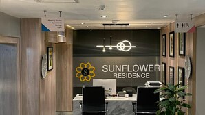 A reception desk with a sign for Sunflower Residence, two black office chairs, a potted plant, and a sign indicating meeting rooms, apartments, lounge, and gym. - Sunflower Residence Victoria Island (Lagos)