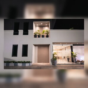 A modern building with a flat facade, multiple windows, and a central entrance. There are potted plants on the ground level and on the balcony. - Sunflower Residence Victoria Island (Lagos)