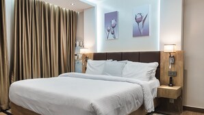 A hotel room with a large bed, wooden headboard, two bedside tables with lamps, and a large window with curtains. - Sunflower Residence Victoria Island (Lagos)