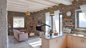 A modern kitchen with a stone wall, a fireplace, and a view of the outdoors. - Mavrabeli Sunset Retreat, with amazing sea and sunset view, 15 minutes from port (Kéa)