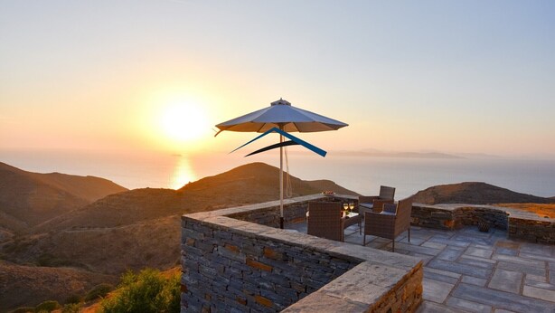 A terrace with stone walls and a table with chairs, overlooking a mountainous landscape at sunset. - Mavrabeli Sunset Retreat, with amazing sea and sunset view, 15 minutes from port (Kéa)