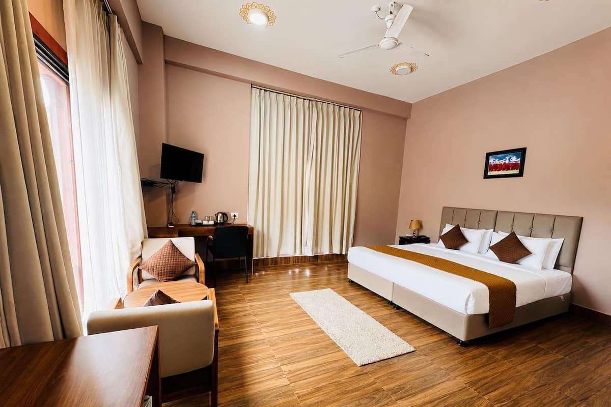 Habitación de hotel con cama, escritorio, silla, televisor y ventana con cortinas.