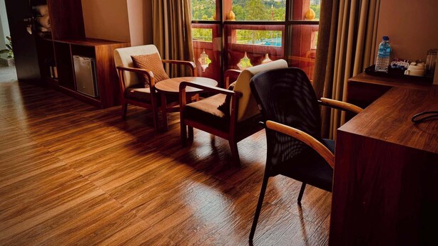 A room with wooden flooring, a desk, two chairs, a refrigerator, and a large window with a view of a mountainous landscape. - Tshongdu Boutique (Paro)