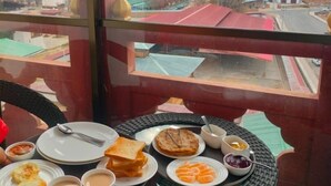 A dining table with plates of food, cups, and a view of a mountainous landscape through a window. - Tshongdu Boutique (Paro)