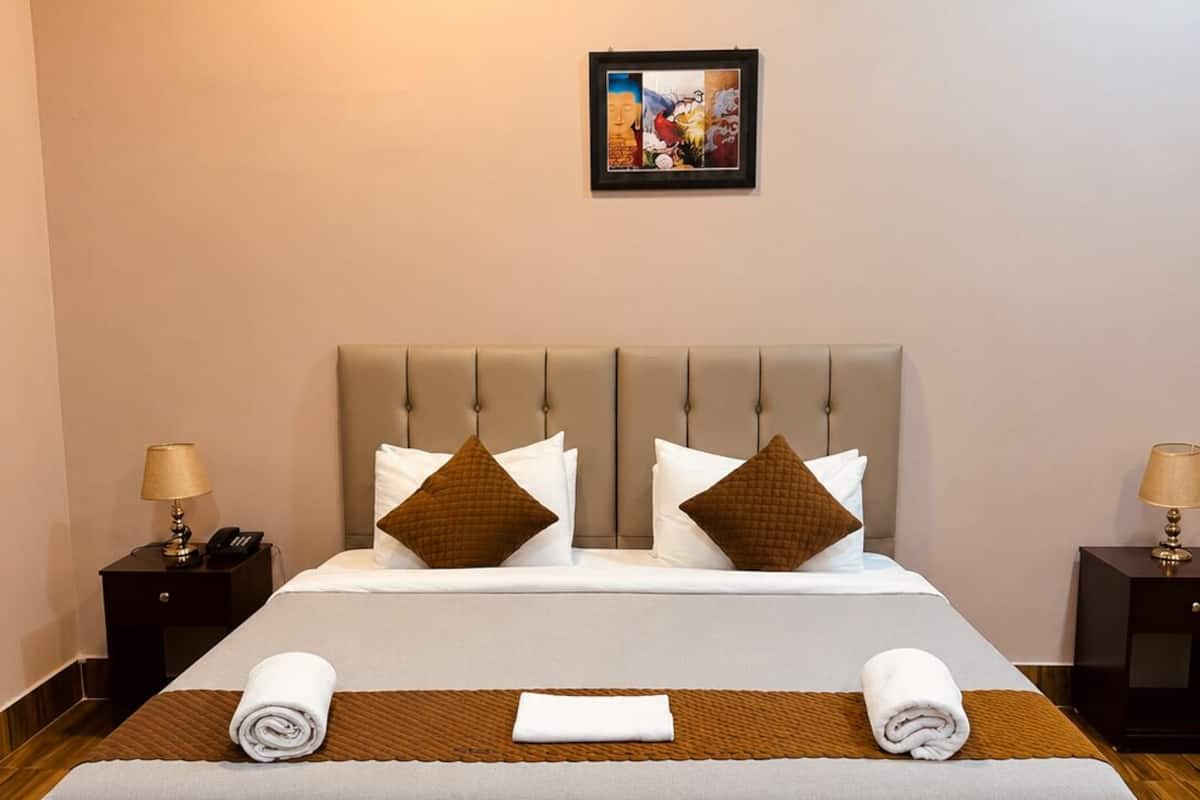 Habitación de hotel con una cama grande, dos mesitas de noche, una obra de arte colgada en la pared y piso de madera.