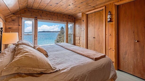 Ein Schlafzimmer einer Holzhütte mit Bett, Nachttisch, Lampe und Blick aufs Meer.