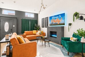 A modern living room with a fireplace, a sofa, a coffee table, and a television displaying 'Welcome To Philly!'
