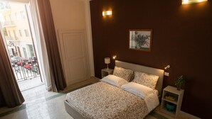 A bedroom with a bed, nightstands, a wall-mounted lamp, and a potted plant.