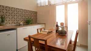 Una cocina con una mesa de madera, sillas, un refrigerador, un fregadero y una ventana con cortinas.