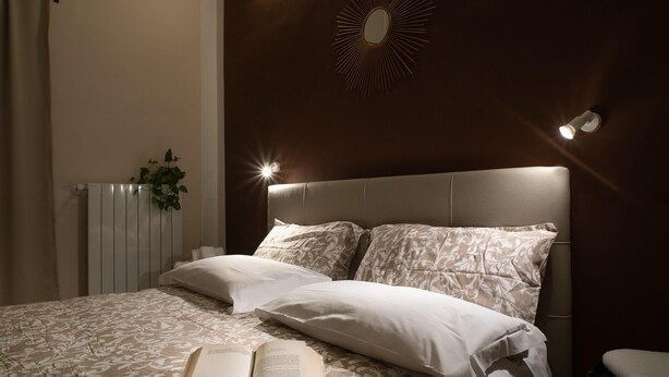 Una cama bien tendida con una colcha estampada, un libro sobre la cama y un espejo fijado a la pared.