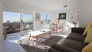 A modern living room with a large window, a sofa, a coffee table, and a dining area. - High Strand 38 by CTHA (Cape Town)