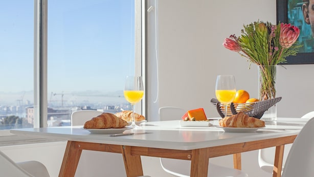 A breakfast table with croissants, orange juice, and a fruit bowl, set against a city view. - High Strand 38 by CTHA (Cape Town)