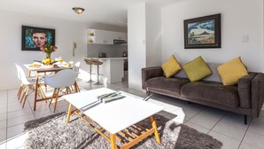 A modern living room with a sofa, a dining table, and a kitchen in the background. - High Strand 38 by CTHA (Cape Town)