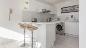 A modern kitchen with white cabinets, a built-in washing machine, and a bar stool. - High Strand 38 by CTHA (Cape Town)