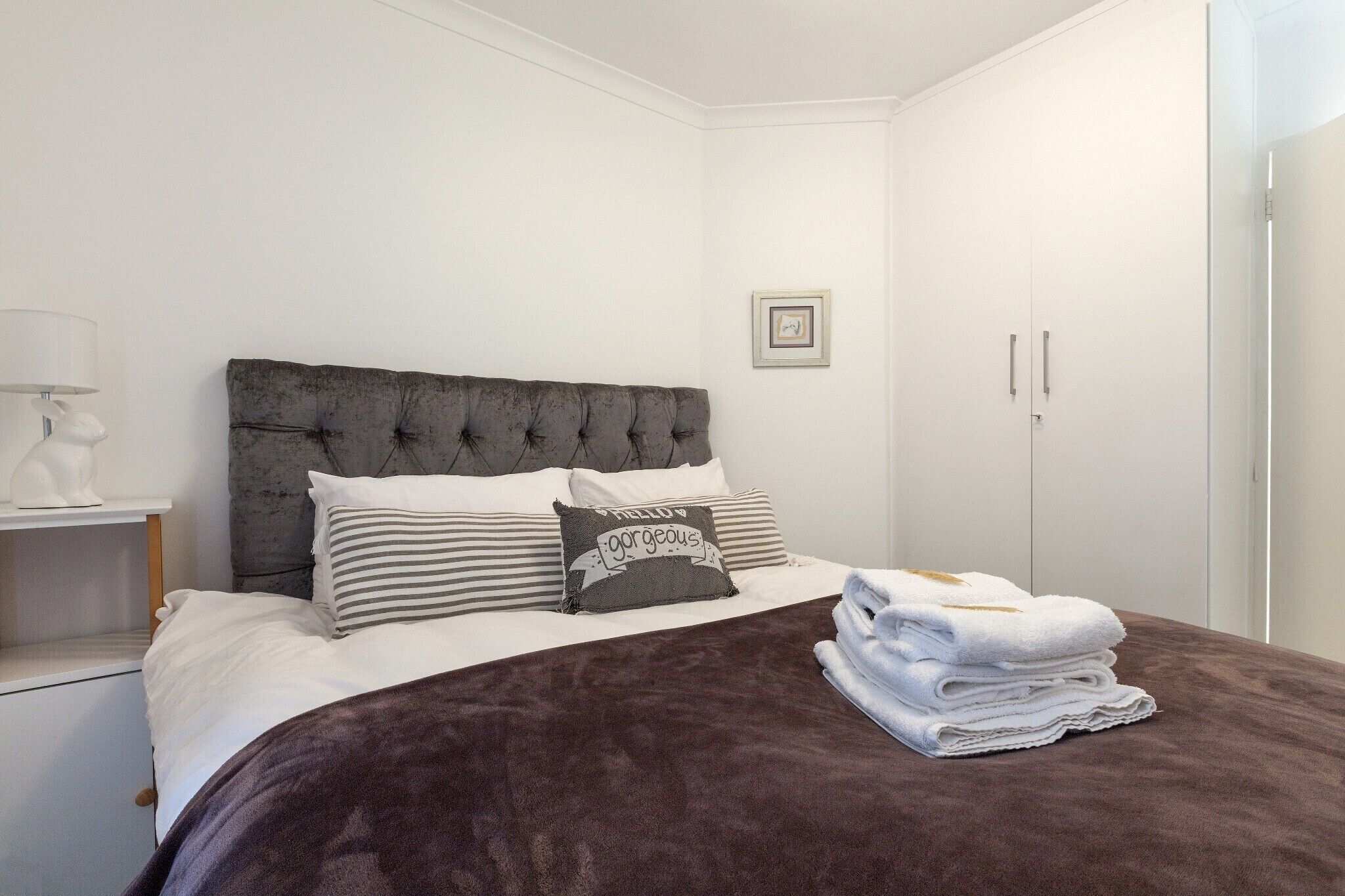A neatly made bed with a dark brown blanket, white pillows, and a decorative pillow with text.