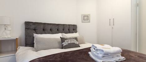 A neatly made bed with a dark brown blanket, white pillows, and a decorative pillow with text.
