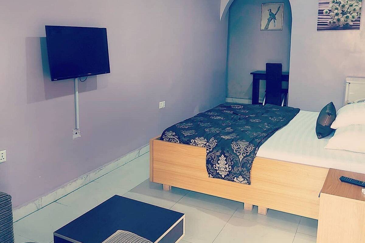 A bedroom with a bed, a TV mounted on the wall, a small table, and a chair.