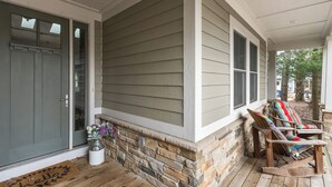 A porch with a stone foundation, wooden floor, and two rocking chairs. - House in the Woods: 4BR Harbert Retreat, 2 Fireplaces, Walk to Beach (Sawyer)