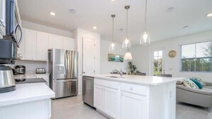 A modern kitchen with white cabinetry, stainless steel appliances, pendant lighting, and a large island. - Modern 3BR Near Disney w Gameroom & Free Waterpark (Davenport)