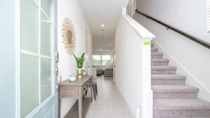 A hallway with a staircase, a desk with a plant, and a decorative mirror. - Modern 3BR Near Disney w Gameroom & Free Waterpark (Davenport)