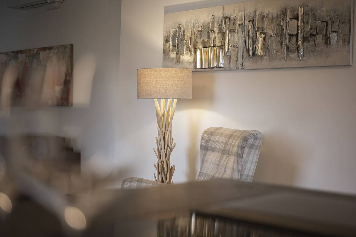 Ein modernes Wohnzimmer mit einer zeitgemäßen Lampe, einem Karo-Sessel und abstrakter Kunst an der Wand.