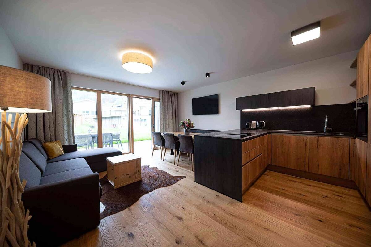 Eine moderne Küche mit Holzausstattung, einer zentralen Kochinsel und einem Essbereich mit einer Couch und Stühlen.