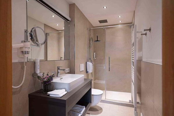 A modern bathroom with a large mirror, a vanity with a sink, a shower area, and a toilet.