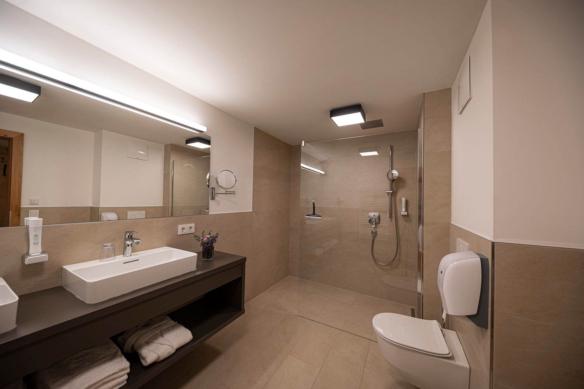 A modern bathroom with a large mirror, a sink, a toilet, and a shower area.
