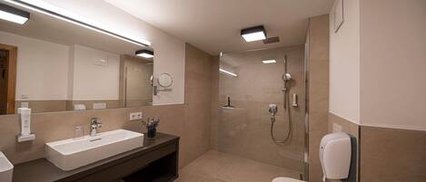 A modern bathroom with a large mirror, a sink, a toilet, and a shower area.