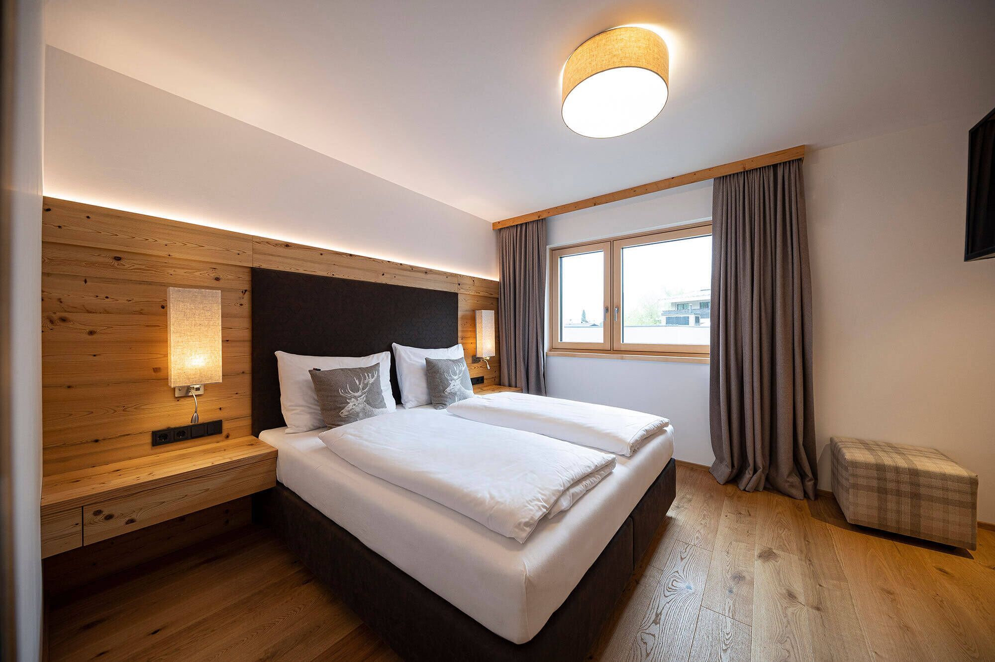 Ett modernt hotellrum med en stor säng, ett träfärgat sänggavel och ett fönster med gardiner.