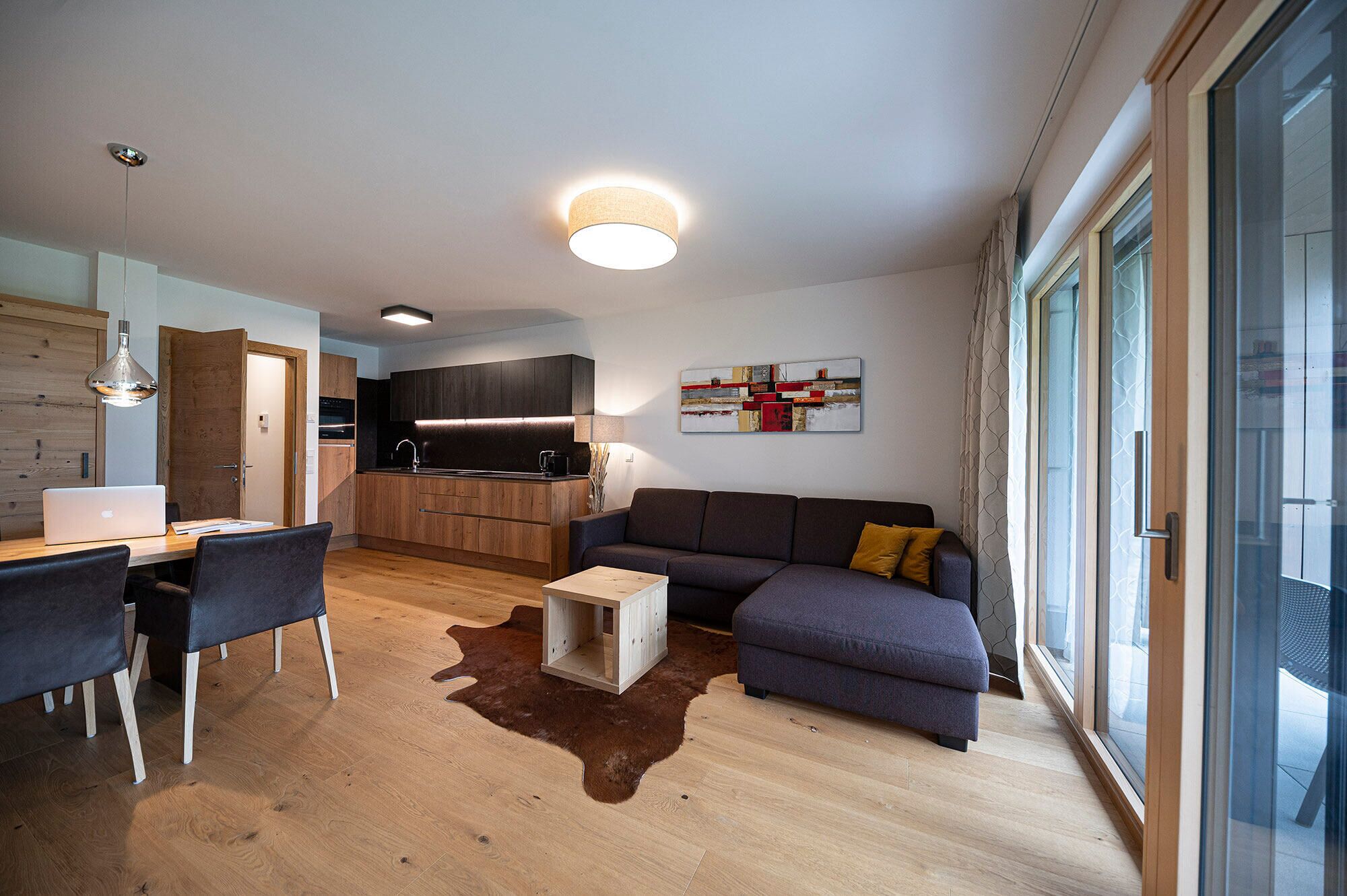 A modern living room with a sofa, a coffee table, and a dining area with a laptop.