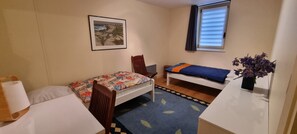 A small, cozy room with a bed, a chair, a desk, and a window.