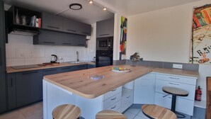 A modern kitchen with dark cabinets, a wooden island with stools, a microwave, and a sink. - REF 410 Bel Appartement de 80m² au Centre de Concarneau (Concarneau)