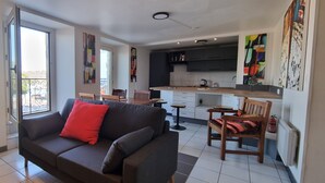 A modern living room with a sofa and chairs, a dining area with a table and chairs, and a kitchen with cabinets and a countertop. - REF 410 Bel Appartement de 80m² au Centre de Concarneau (Concarneau)