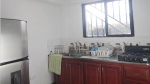 A compact kitchen with a stainless steel refrigerator, a gas stove, wooden cabinets, and a window with blinds. - Piso 1. Hermoso Amanecer Frente al Embalse! (Peñol)