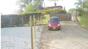 A red car parked on a gravel driveway leading to a gated entrance with a wooden fence and a house in the background. - Piso 1. Hermoso Amanecer Frente al Embalse! (Peñol)