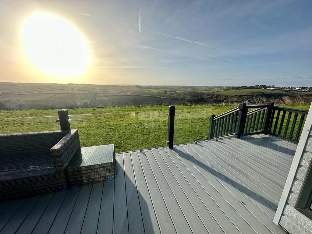 A wooden deck with a view of a green landscape and a clear sky.
