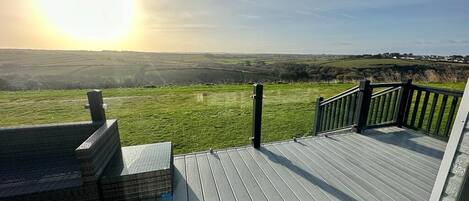A wooden deck with a view of a green landscape and a clear sky.