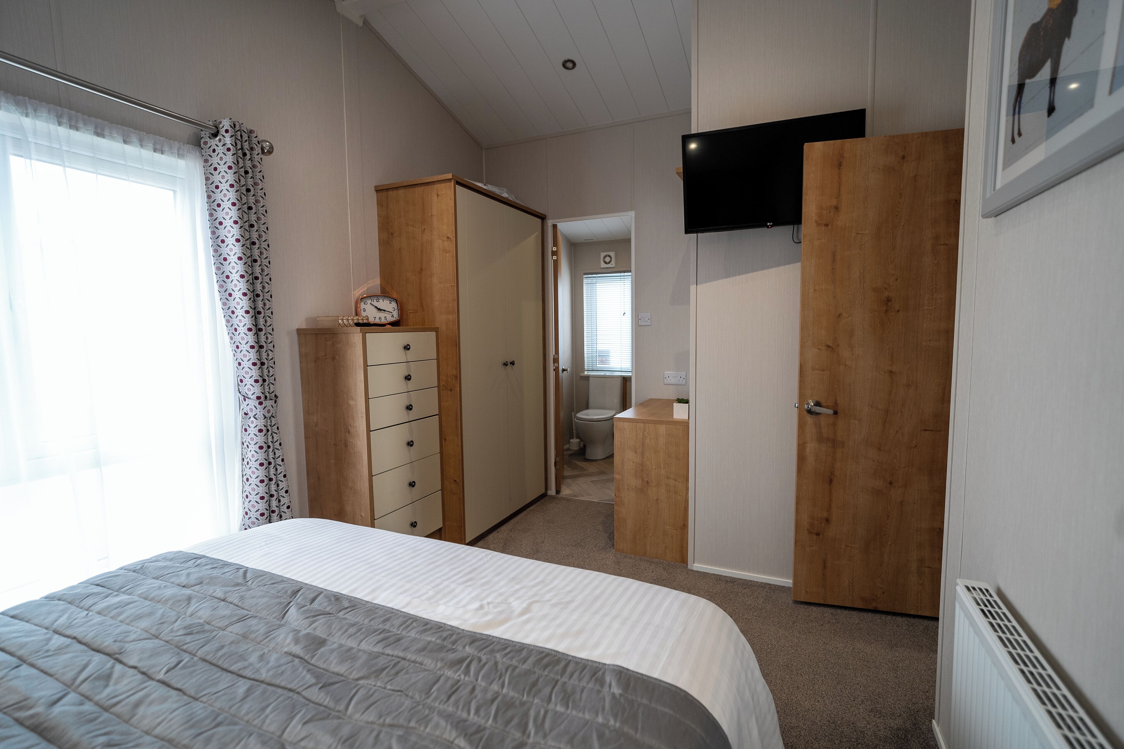 Une chambre à coucher avec un lit, une armoire, une télévision et, au fond, une salle de bain.
